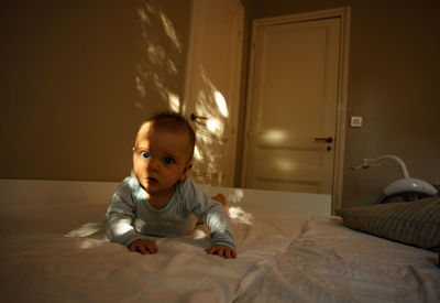 Portrait of cute baby boy sitting on bed at home