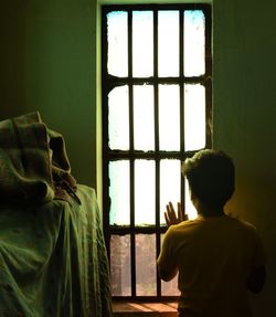 Rear view of man looking through window at home