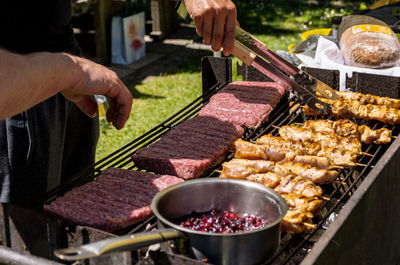 Close-up of man holding utensil and grilling meat in back yard.