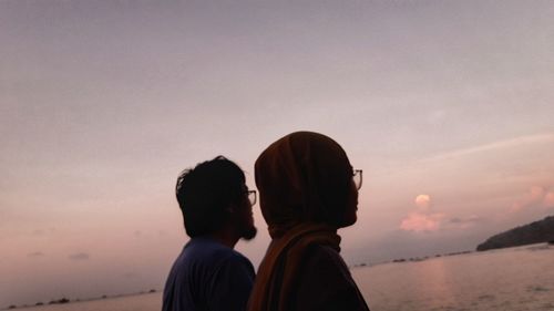 Rear view of man and woman against sea during sunset