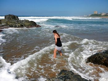 Full length of young woman standing on beach against sky