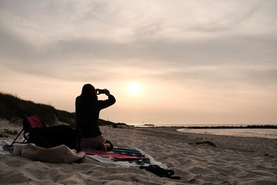 Man using mobile phone at beach against sky during sunset