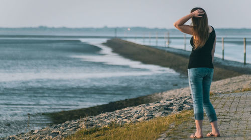 Rear view of woman standing at beach against sky