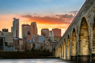 River amidst buildings against sky during sunset