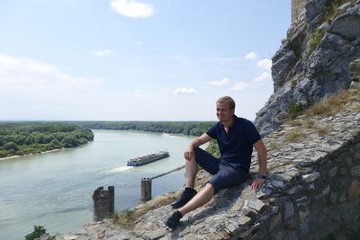 Young man sitting on retaining wall against sky