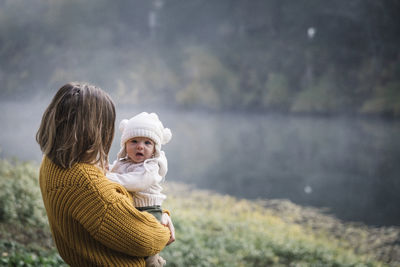 A woman is holding a baby near a river