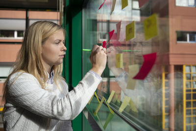 Woman making notes on post it sticker to window