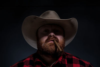 Portrait of mature man wearing hat smoking cigar against black background