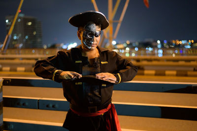 Portrait of young man wearing pirate costume standing on bridge at night