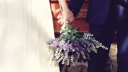 Cropped image of bride and groom holding bouquet