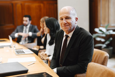 Portrait of smiling senior male lawyer in board room with colleagues during meeting