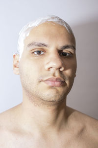 Portrait of shirtless bald man with shaving cream on head standing against wall