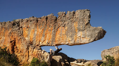 Man climbing rock against blue sky