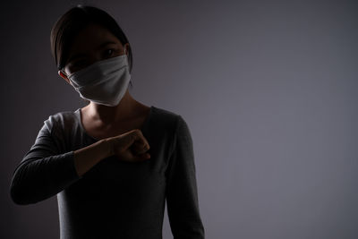 Portrait of young woman standing against black background