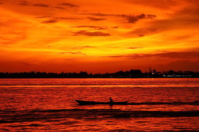 Silhouette man in sea against orange sky