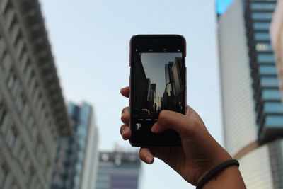 Cropped hand photographing buildings through mobile phone