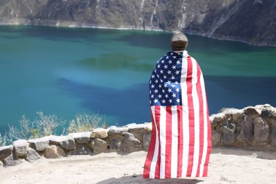 Rear view of man with american flag standing by lake