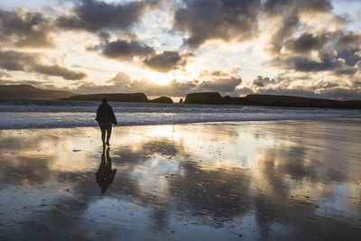 Rear view of man on beach against sky during sunset