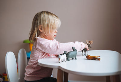 Little girl toddler playing with animal toys on table in children's room at home