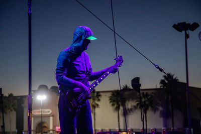 Man standing against illuminated street light against blue sky