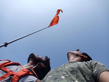 Low angle view of friends looking at flag waving against clear sky