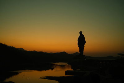 Rear view of man standing at beach against sky during sunset