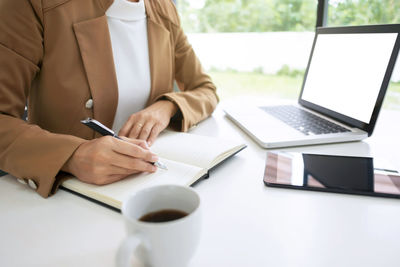 Midsection of woman using mobile phone while sitting on table