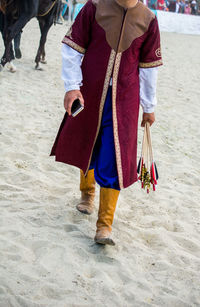 Low section of man with arrow bows walking on sand