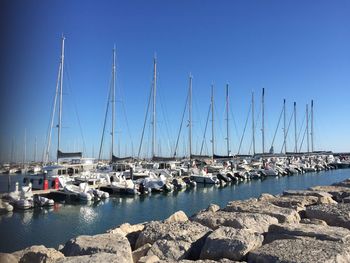 Sailboats moored in harbor against clear blue sky