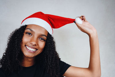 Portrait of smiling young woman wearing santa hat sitting against wall