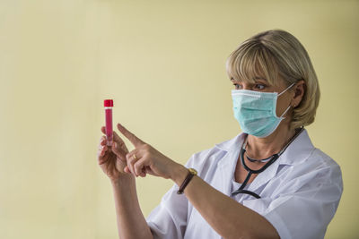 Doctor wearing mask holding test tube against yellow background