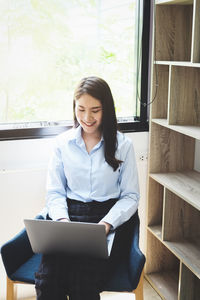 Young woman using phone while sitting on window