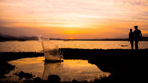 Silhouette people standing on beach against sky during sunset