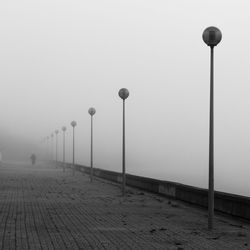 Street lights on footpath in city against sky