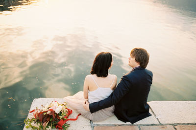 Side view of woman sitting on rock by lake