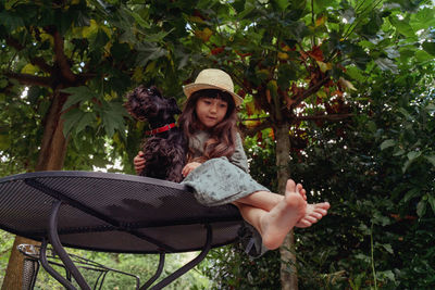 Low angle view portrait of girl sitting on table with little black dog