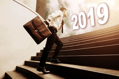 Digital composite image of businessman with suitcase moving up on steps towards numbers against cloudy sky