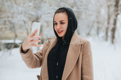 Young woman using phone while standing on snow