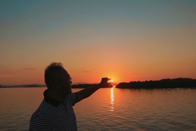 Woman standing by lake against sky during sunset