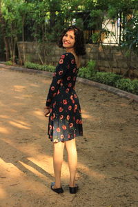 Portrait of smiling young woman standing against trees