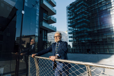 Senior businessman with eyeglasses standing outside office building by railing