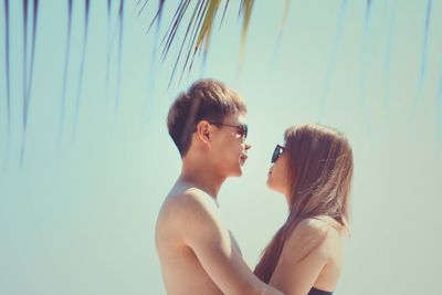 Side view of young romantic couple against sky on sunny day