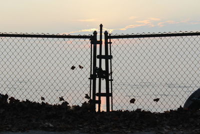 Silhouette fence against sky during sunset