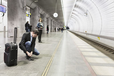 Businessman tying shoelace while waiting at railway station