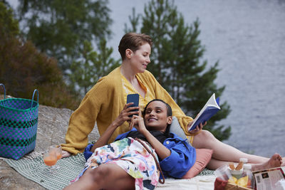 Female couple having picnic, reading book, and using phone