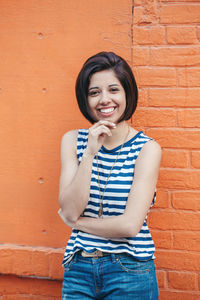 Portrait of smiling young woman standing against wall