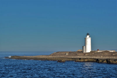 Lighthouse by sea against clear sky