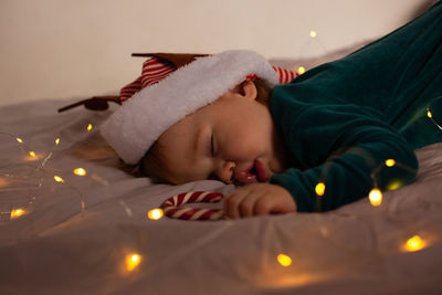 Little baby lies on the bed in a christmas costume and a hat with deer antlers. 