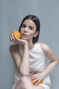 Young woman holding orange fruit against blue background