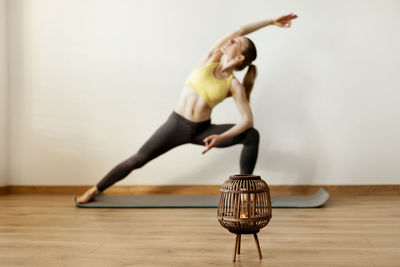 Close-up of oil lamp on floor with woman exercising in background against wall